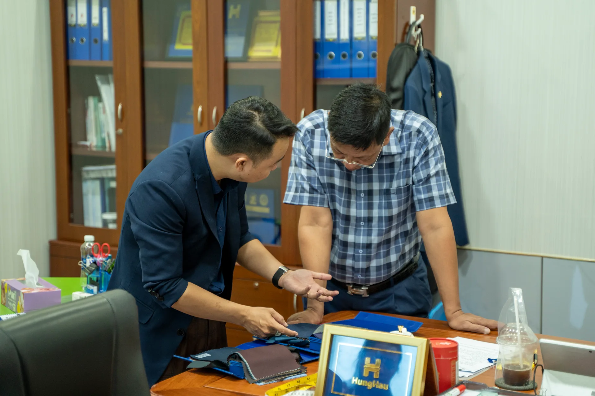 A Mon Amie advisor discussing suit fabrics with a company leader, a company logo frame on the table