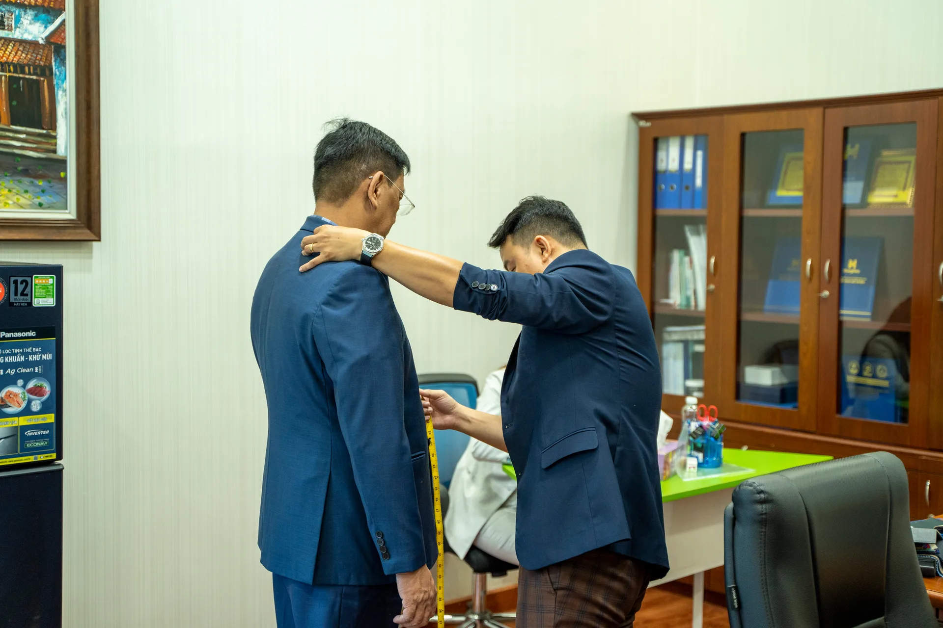 Measuring the back and shoulders on a blue suit jacket to adjust the fit for a leader