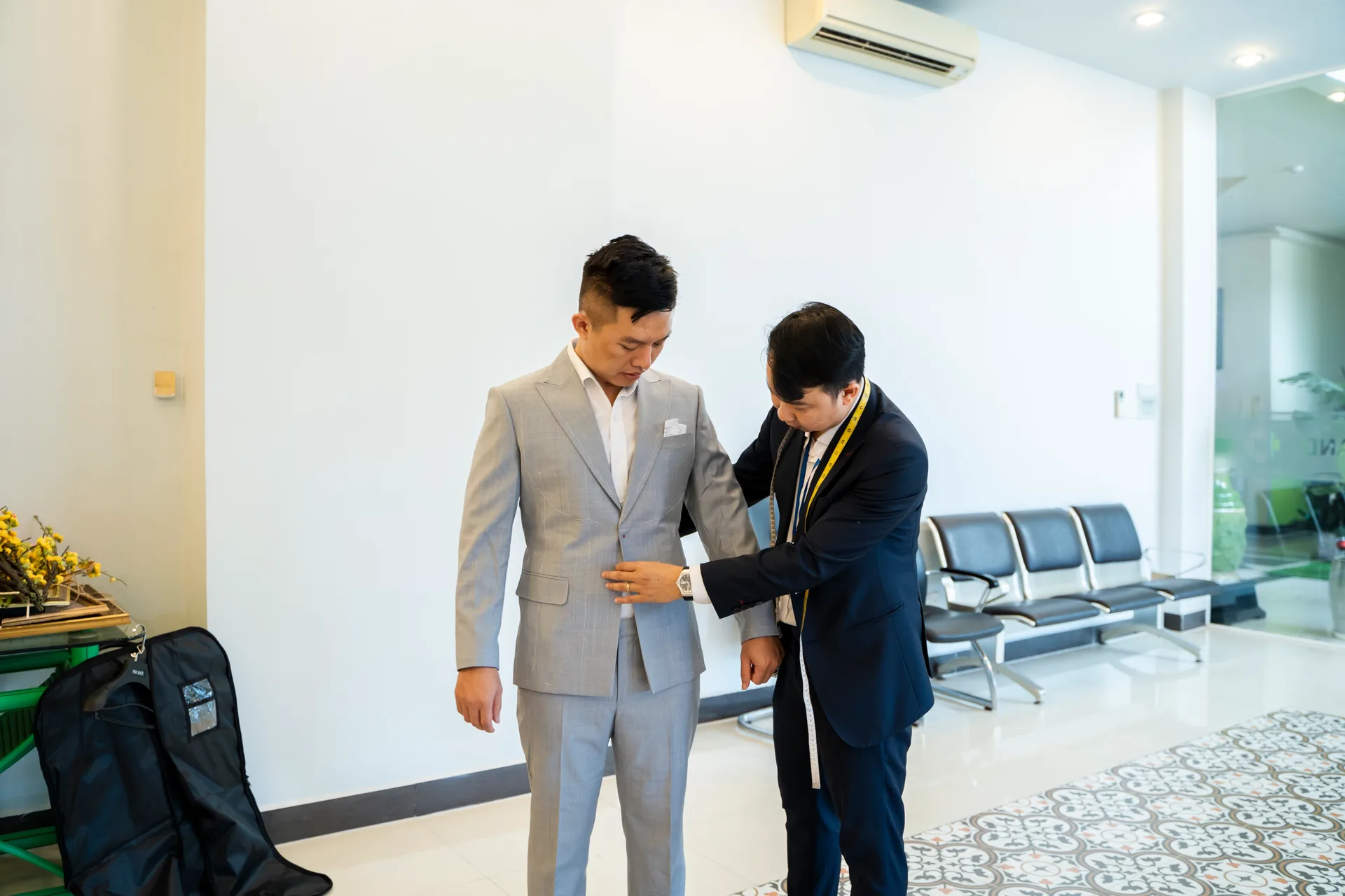 Adjusting a grey suit jacket on a male employee, with a yellow measuring tape draped over the specialist's shoulder