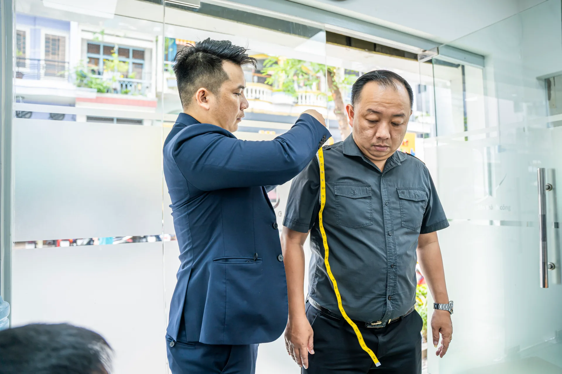 Nhân viên nam được đo chiều dài áo bằng thước dây vàng khi may đồng phục veston