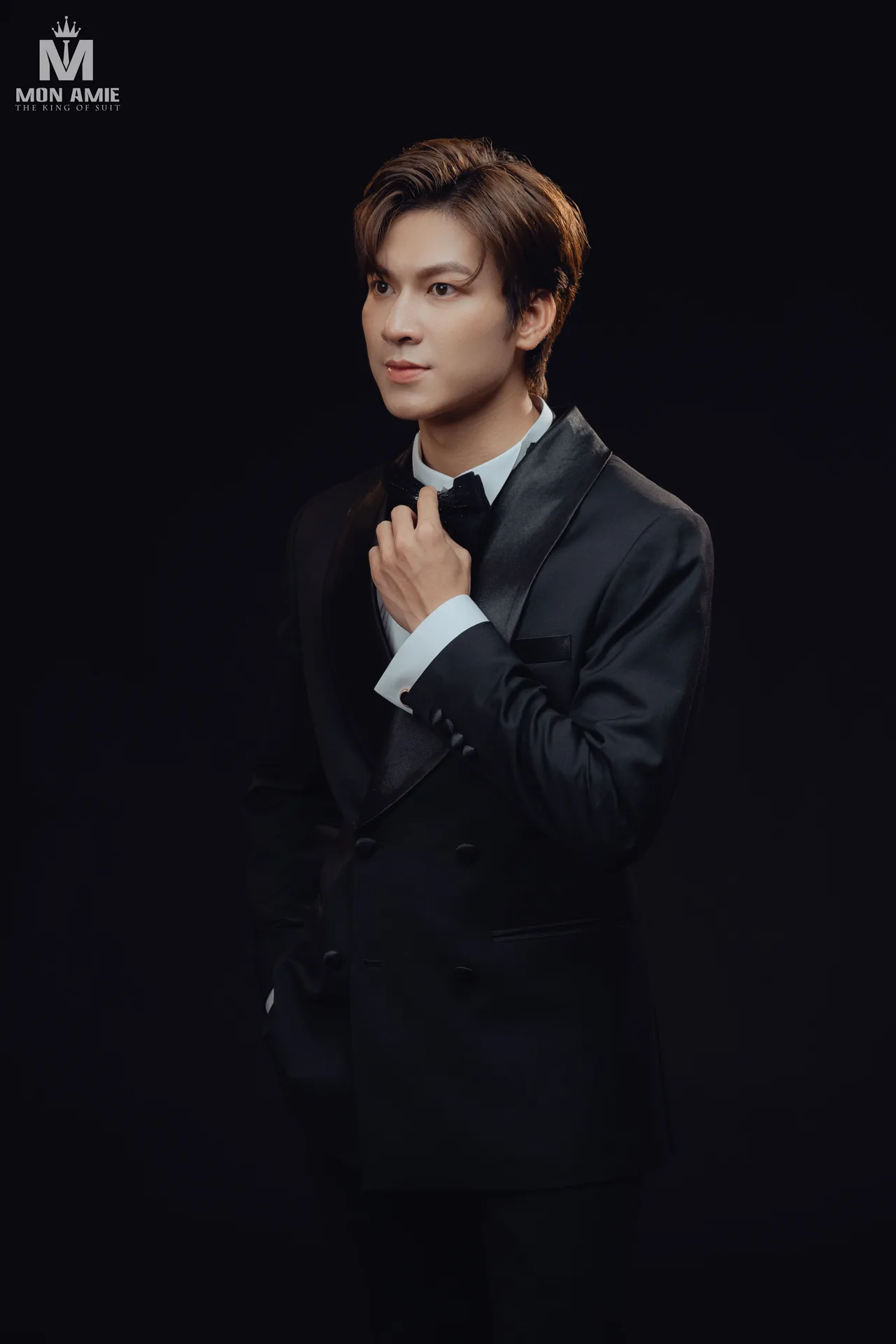 Tuxedo đen cài nơ, cổ ve satin trên nền studio tối, minh họa ve satin và nơ của áo tuxedo nam