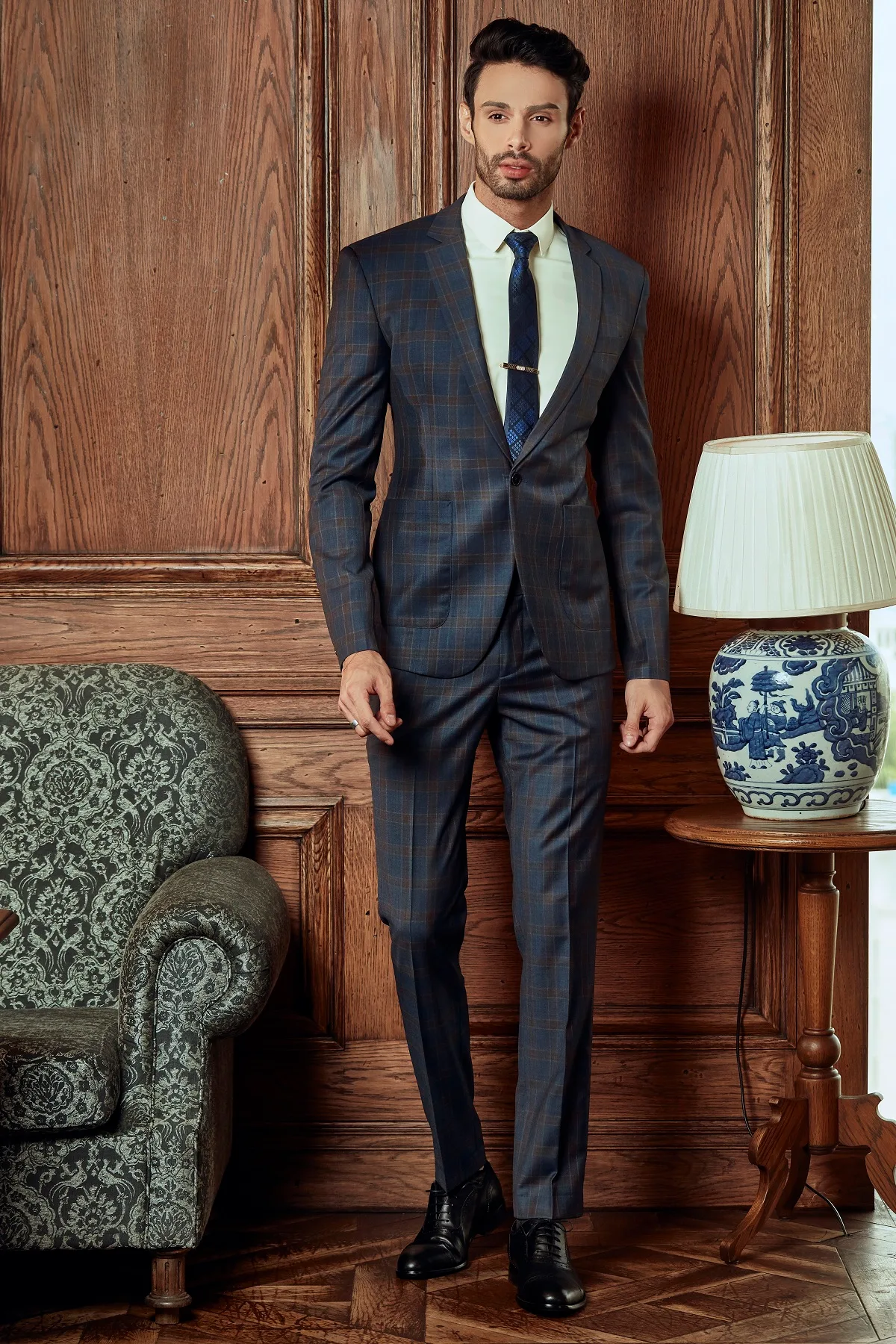 Suit kẻ ô xanh than, cà vạt kẹp tinh tế, bên bình gốm xanh trắng, minh họa vest nam xanh than