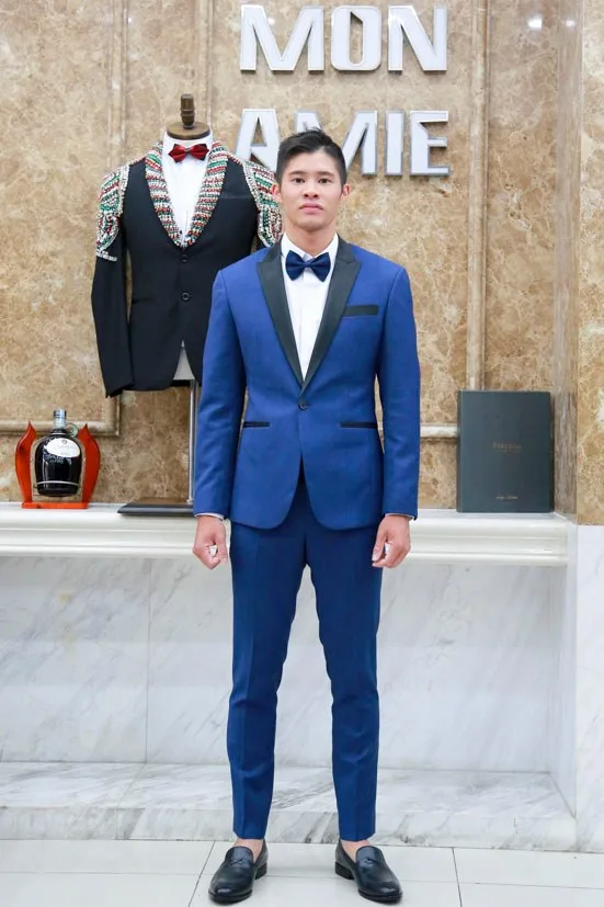 Chú rể trong tuxedo xanh coban cổ lụa đen, nơ đen sang trọng trước logo Mon Amie