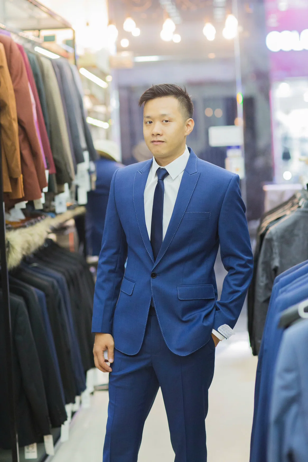 Nam vest xanh dương chỉ nổi, cà vạt navy, đứng thẳng phong thái tự tin để kiểm tra vai và độ dài áo