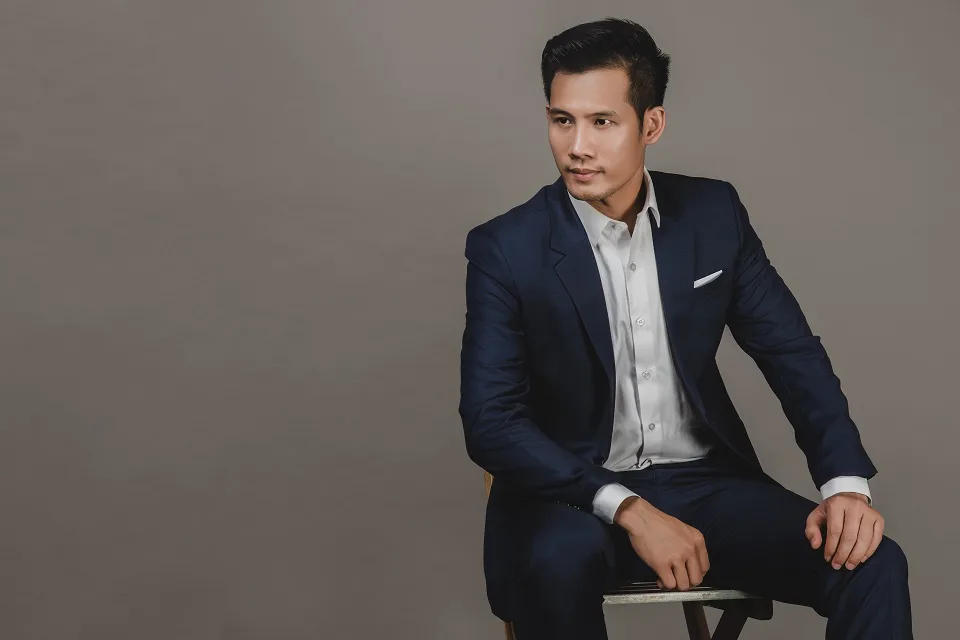 Suit kem ba mảnh cài khuy vàng, sơ mi mở cổ bên tủ gỗ, hình ảnh vest không cà vạt vẫn sang trọng