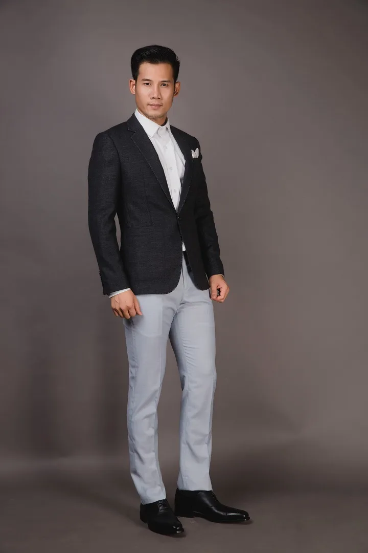 Black tuxedo with silk lapels and bow tie, standing with arms folded between rows of carved wooden columns