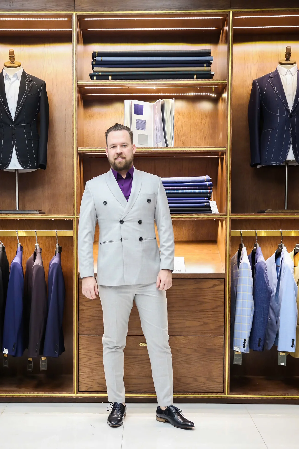 Quý ông vest xám sáng, sơ mi tím trong showroom gỗ, hình ảnh khách quốc tế trải nghiệm may đo tại Mon Amie