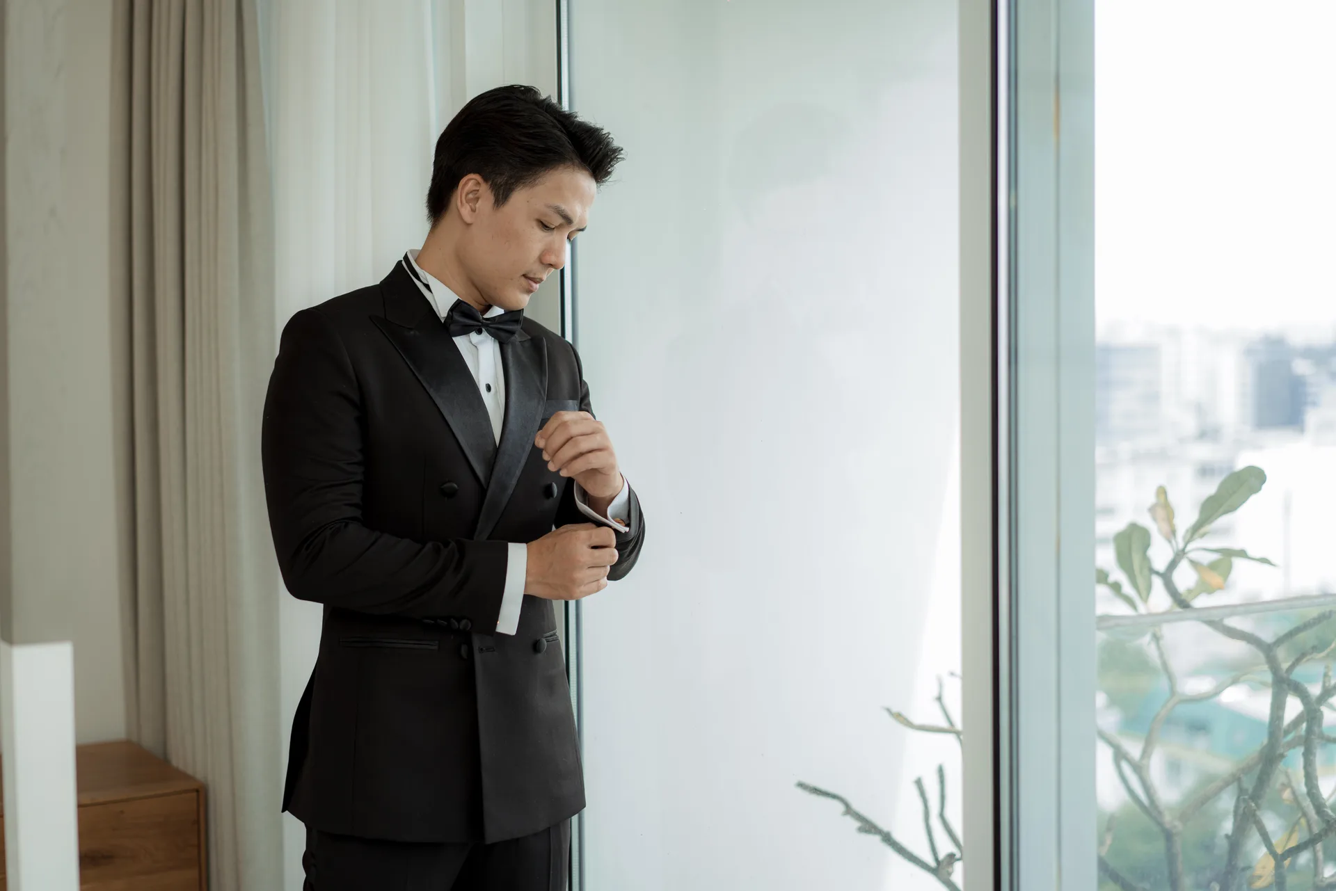 Chỉnh măng sét tuxedo bên cửa kính, dáng đứng thanh lịch