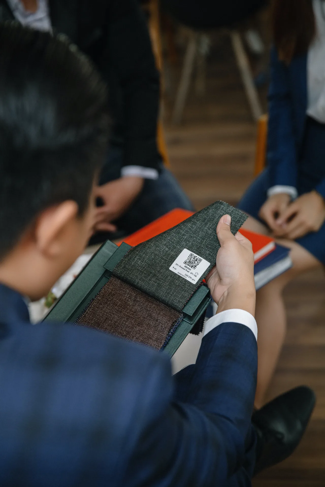 Cận cảnh bàn tay chạm mẫu vải len lụa trong sổ mẫu, một trong các loại vải may vest cao cấp