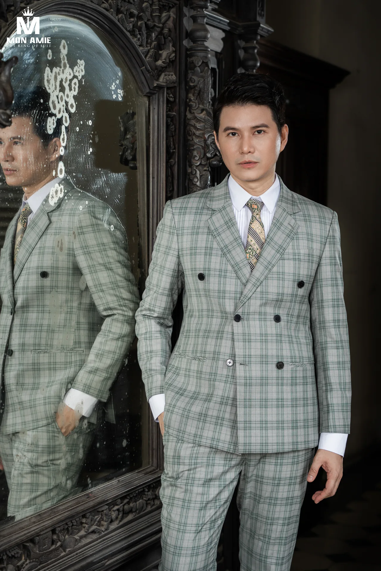 Green check double-breasted suit beside a mirror in a carved wooden frame