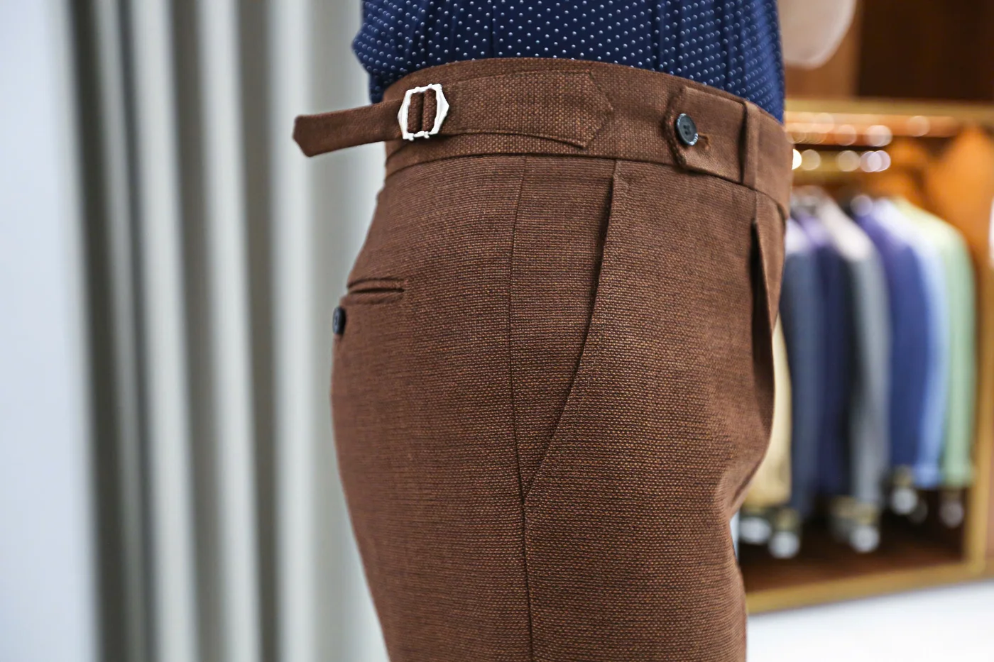 Close-up of brown woven trousers with an adjustable waist buckle, a waistband detail to note when measuring