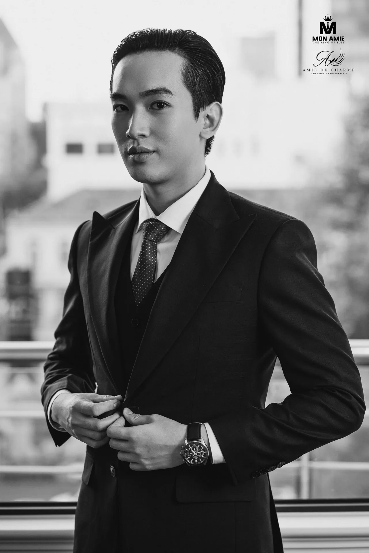 Black monochrome three-piece, black-and-white photo, both hands buttoning the suit jacket