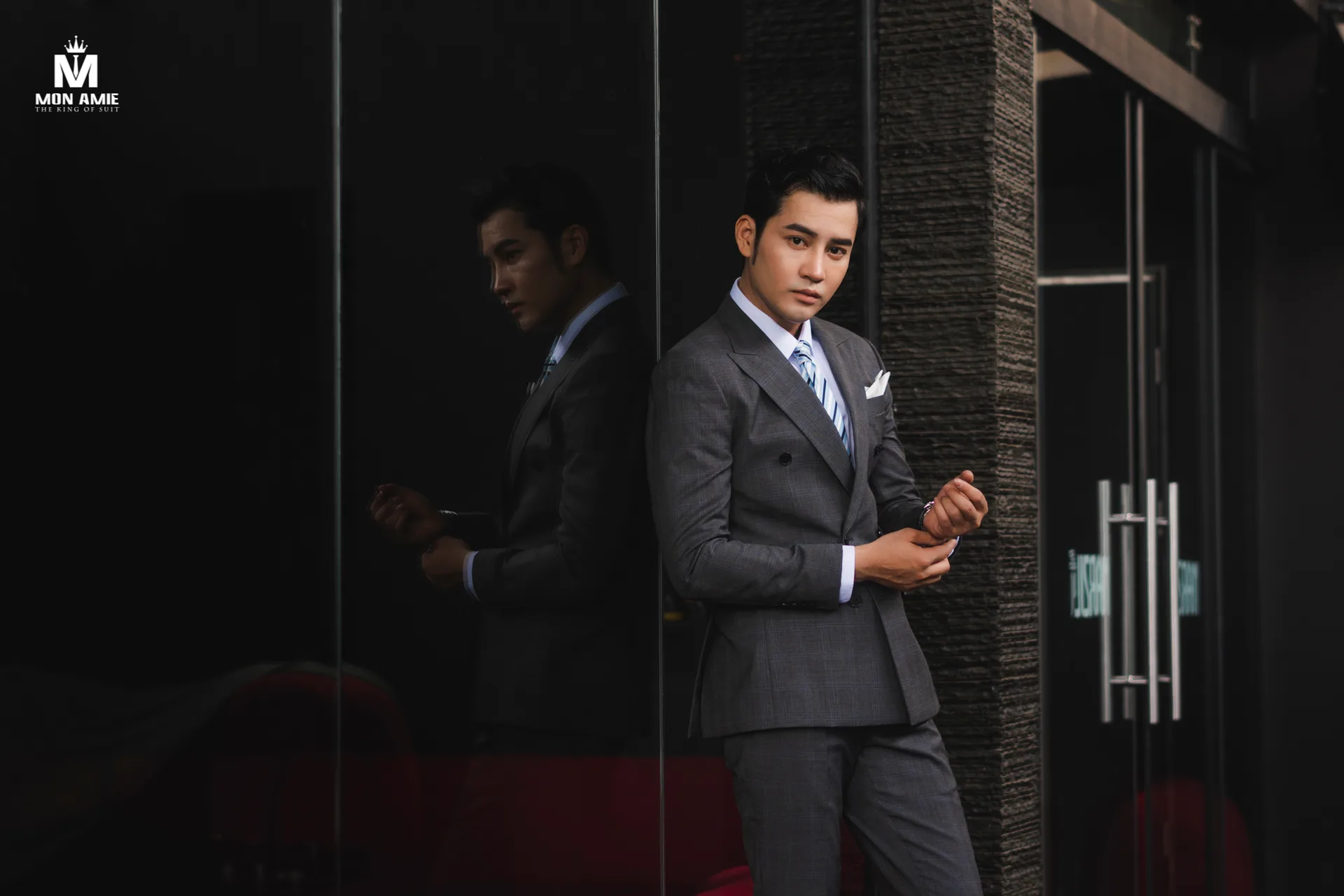 Coffee-brown waistcoat and trousers with a matching tie against a white wall, an example of a waistcoat-and-trouser set in one colour
