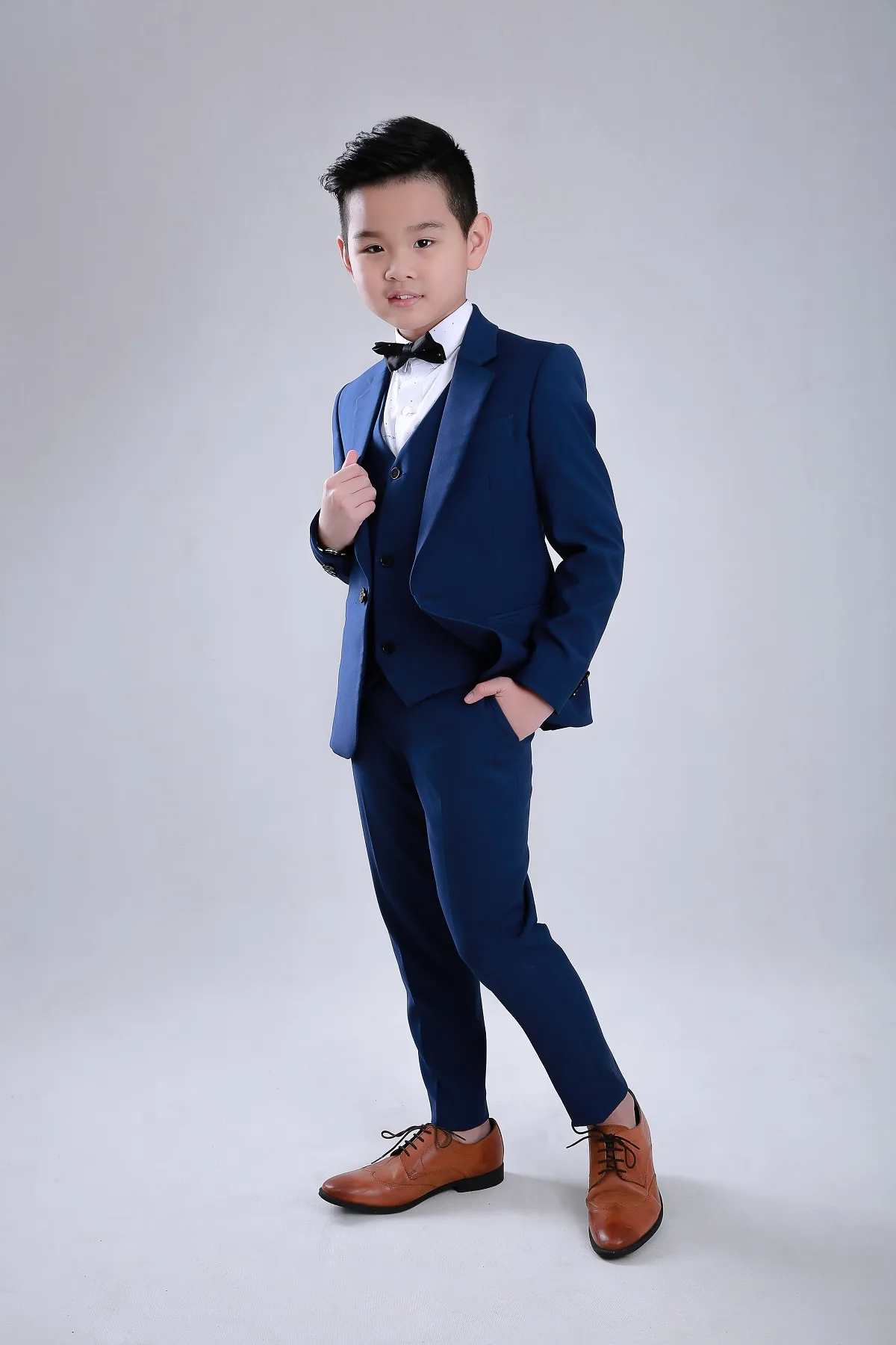 Bé đứng chéo trong vest navy ba mảnh cùng giày da nâu