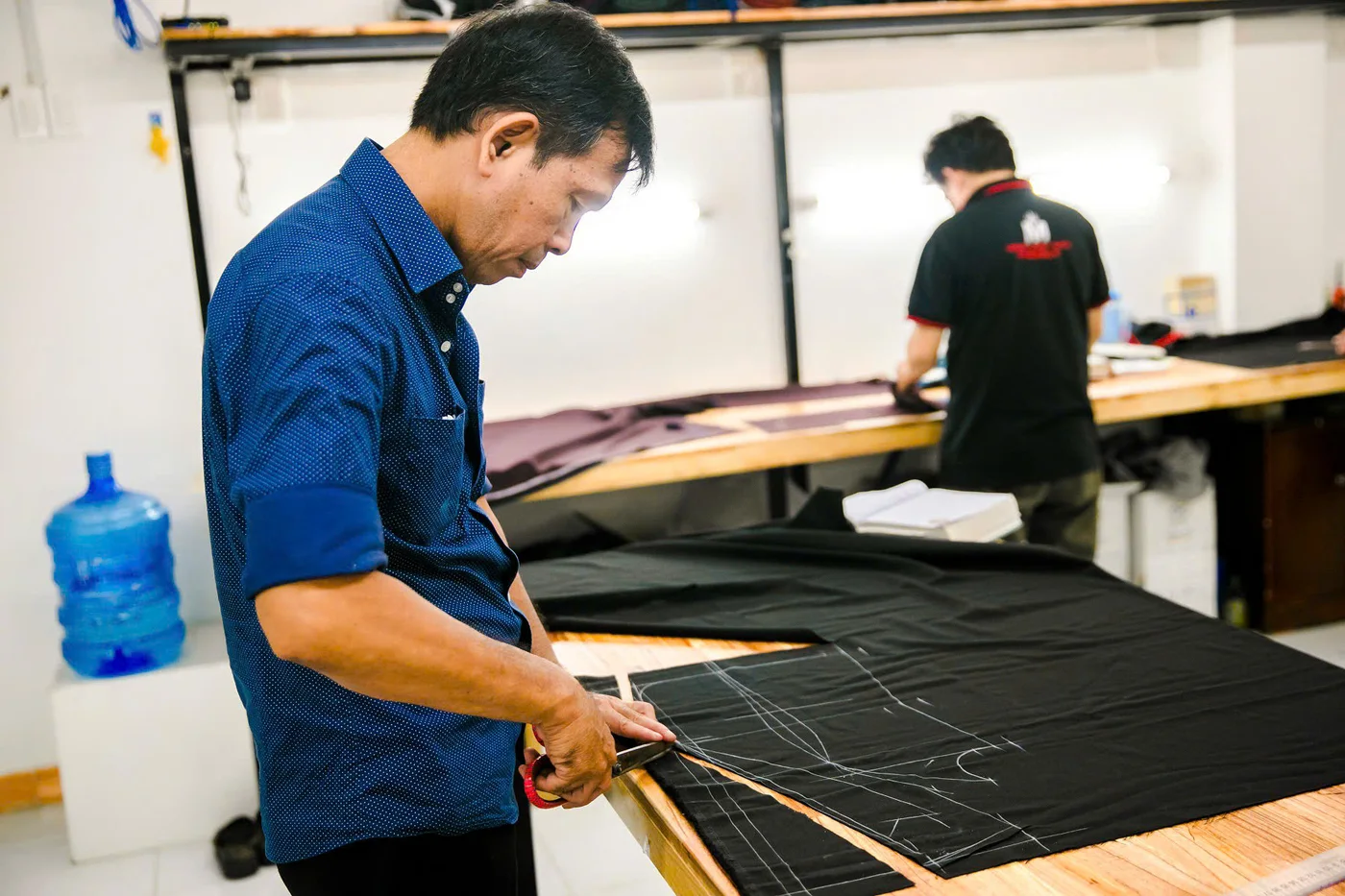 Thợ cả áo sơ mi xanh navy cắt vải đen trên bàn gỗ